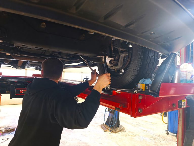 Technician working under a vehicle raised on a lift at Tech Savvy Automotive