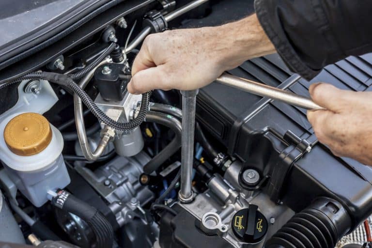 Two hands using wrenches to tighten a bolt in an engine bay
