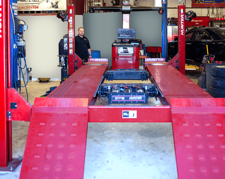 Technician beside the Hunter four-post alignment rack in the service bay