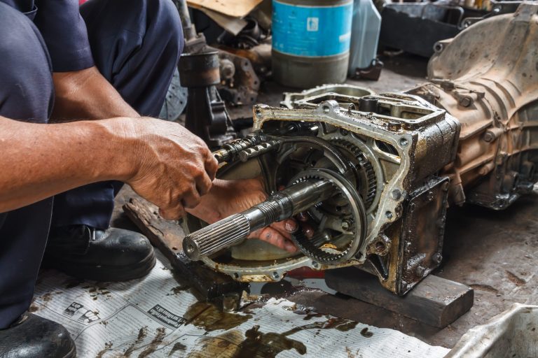 Two people working on a disassembled transmission on a shop table