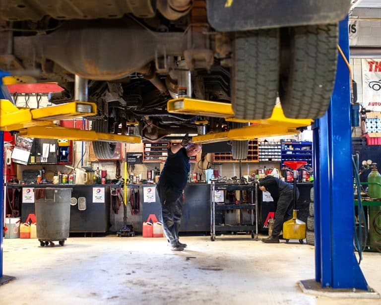 Technicians working beneath a vehicle on a two-post lift