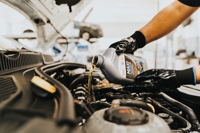 Gloved hand pouring oil from a marked bottle into an engine