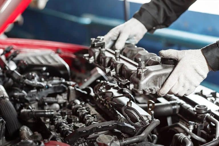 Gloved hands lifting a cylinder-head cover from an engine bay