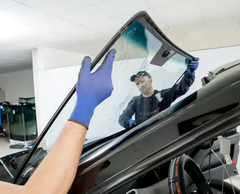 Hands holding a new windshield panel in a shop