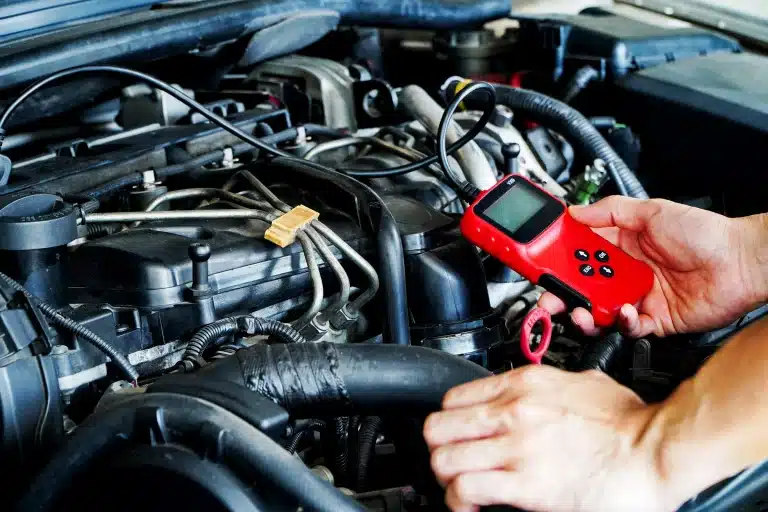 Hand holding a red OBD-II diagnostic scanner plugged into an engine bay