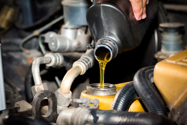 Close-up of oil pouring from a bottle into an engine reservoir