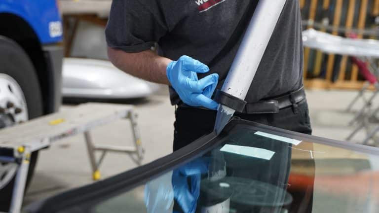 Red-gloved hands using a trim tool on a windshield edge