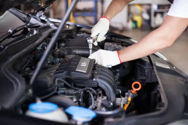 Gloved hand using a ratchet on an engine under an open hood