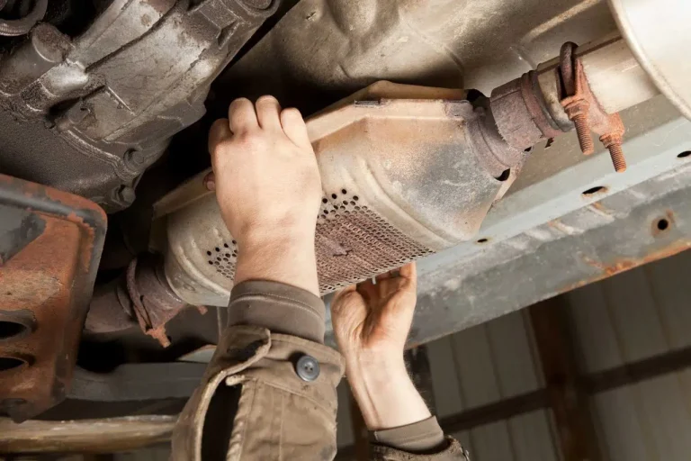 Hand holding a catalytic converter under a vehicle