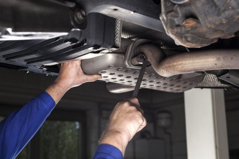 Hands using a wrench on a muffler under a lifted vehicle
