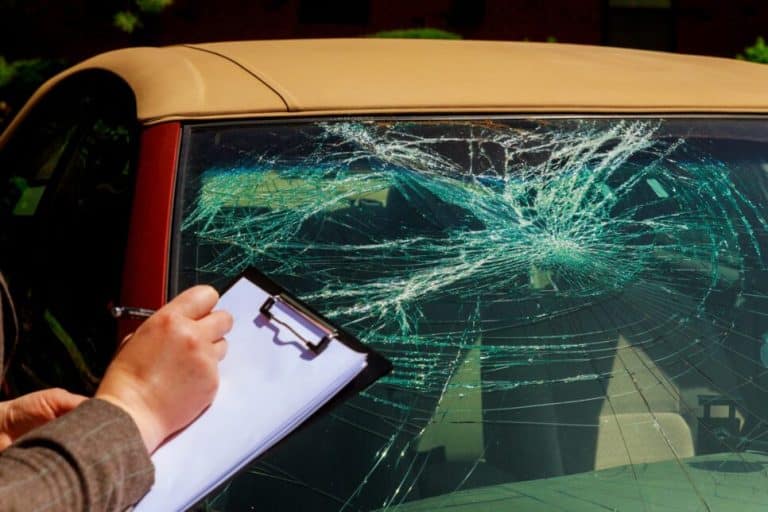 Cracked windshield in the foreground with a hand writing on a clipboard behind