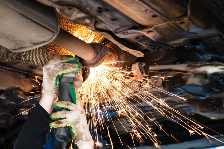 Worker cutting an exhaust pipe with an angle grinder, sparks flying