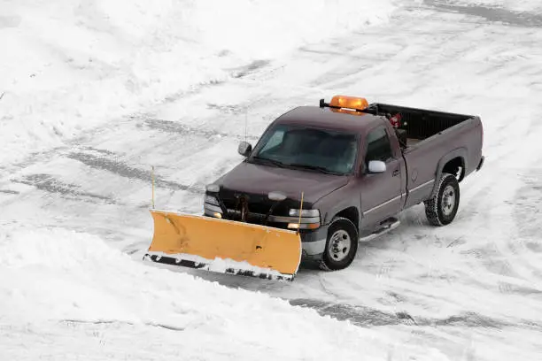 Maroon pickup with a yellow plow blade clearing a snowy lot
