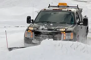 White pickup with a roof light bar pushing snow