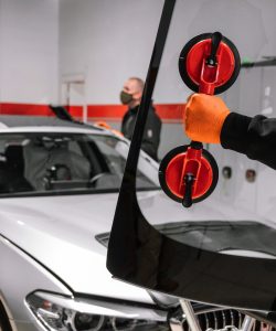Technician using suction tools on a sedan windshield in a garage bay