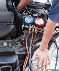 Hand holding a red and blue AC gauge set near an open engine bay