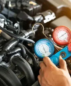Hands holding an AC gauge manifold connected to engine bay hoses