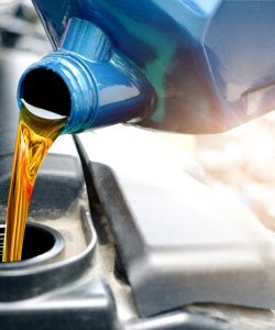 Oil pouring from a blue jug into an engine in sunlight