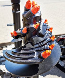 Auger drill bit with orange safety caps on pavement