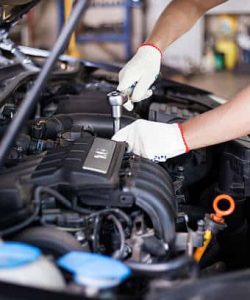 Gloved hands using a wrench in an open engine bay