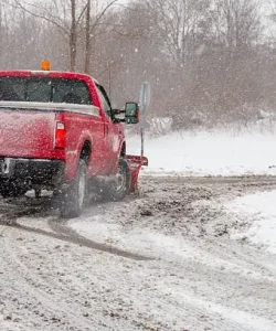 Red pickup with a plow blade driving through a snowstorm