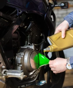 Oil poured through a green funnel into a motorcycle engine