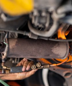 Worker torch-welding an exhaust pipe under a vehicle