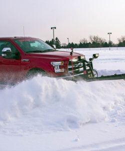 Pickup truck with a plow blade clearing snow from a parking lot at dusk