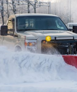 Pickup truck pushing snow with a red plow blade on a winter street