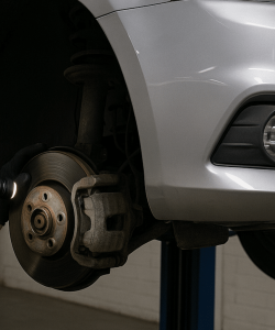 Gloved hand using a tool on a brake rotor under a raised car